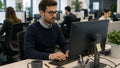 Un impiegato lavora al computer nella propria postazione in un openspace, colleghi sullo sfondo